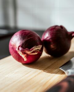 Close-up shot of fresh red onions on a wooden chopping board under sunlight, perfect for cooking themes.