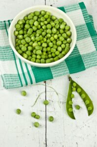 A vibrant display of green peas in a bowl with a rustic white background, ideal for food and health concepts.